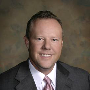 DR. John R. Molland wearing a black jacket, white shirt, and pink tie